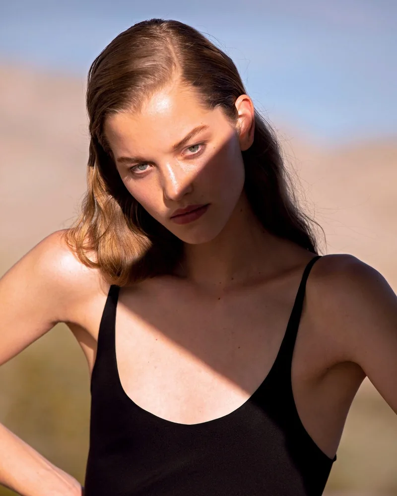 A model in a black camisole looking toward the camera in warm sunlight.