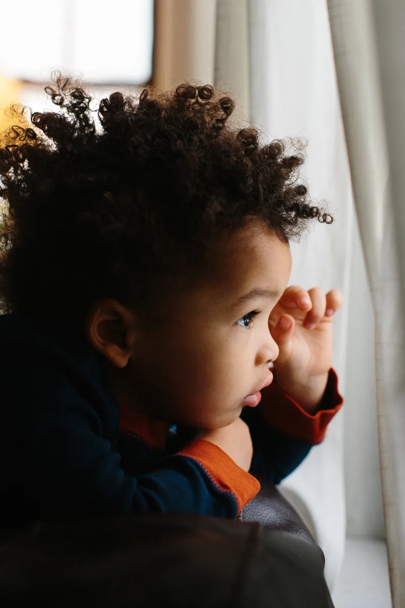 A child looking out of a window with one hand near the glass.