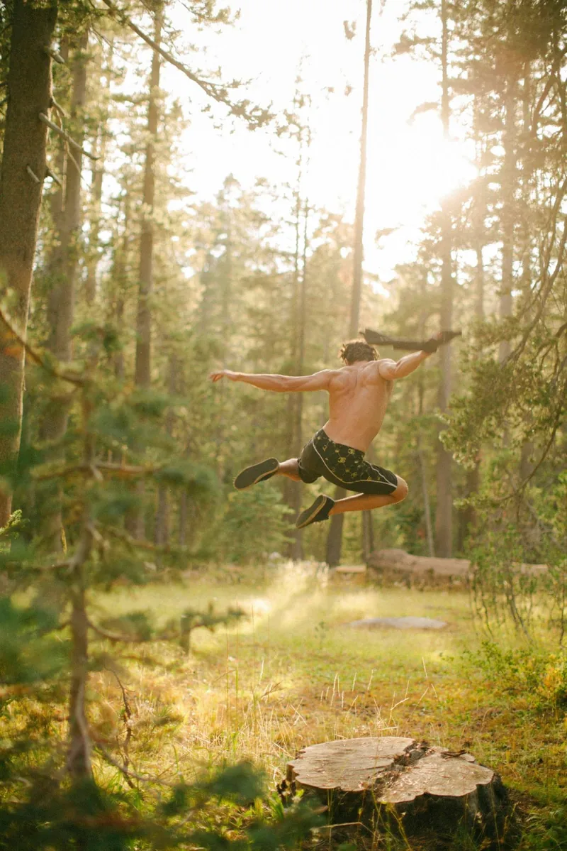A person leaping through a sunlit clearing in the woods.