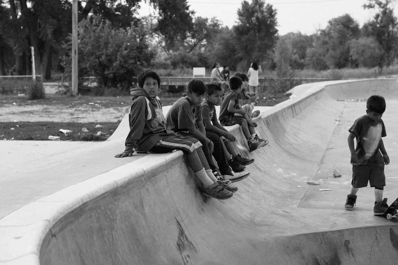 Children sitting along the edge of a concrete skate bowl, in black and white.