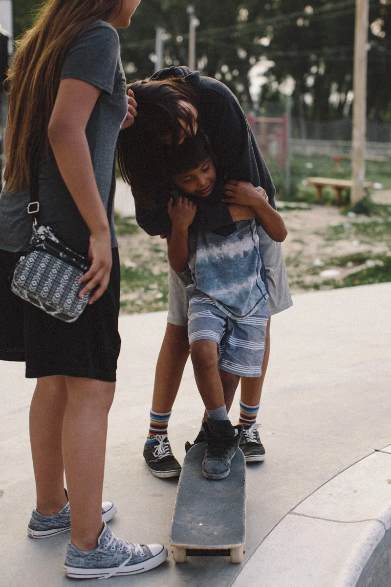A child standing on a skateboard with two people nearby at a skate park.