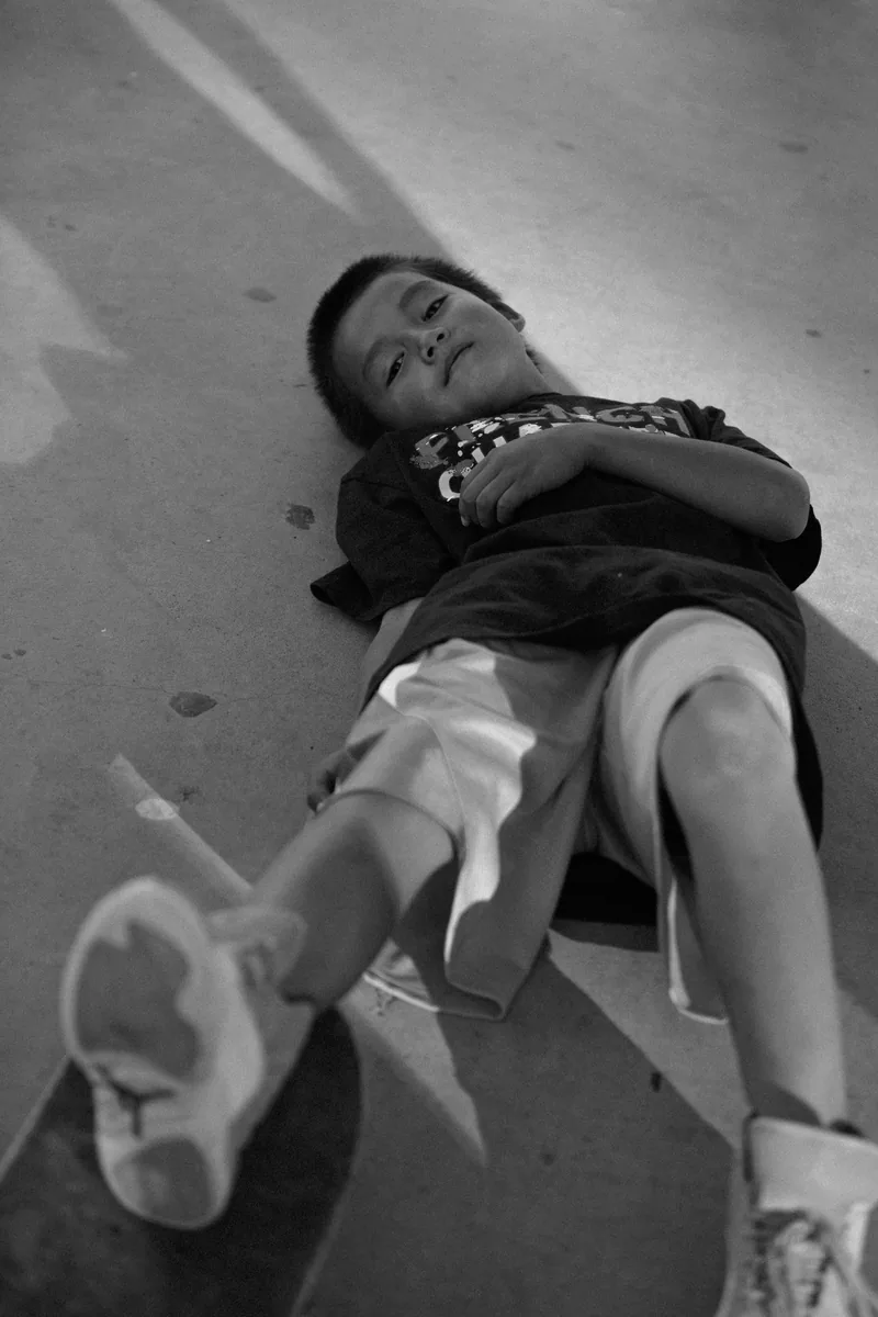 Black-and-white photograph of a child lying back on a concrete skate ramp.