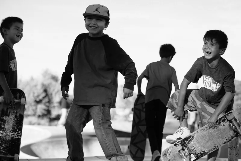 Children laughing and holding skateboards at a skate park, in black and white.