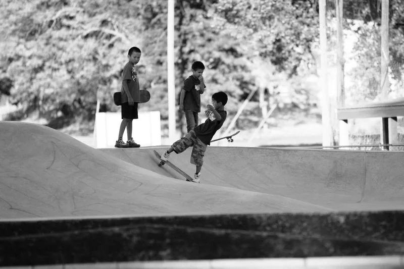 Children skating and watching from the edge of a concrete ramp, in black and white.